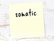 Yellow sticky note on wooden wall with handwritten word somatic