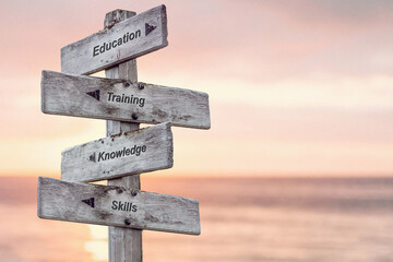 education training knowledge skills text written on wooden signpost outdoors at the beach during sunset