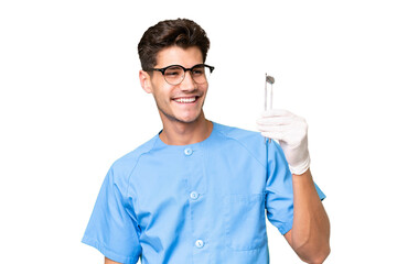 Wall Mural - Young dentist man holding tools over isolated background looking to the side and smiling