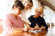 © Татьяна Волкова - Young smiling woman businesswoman standing behind two elderly women sitting at desk, explaining business plan in office.