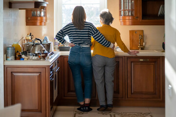 Wall Mural - Daughter and her old mother stands near the window and hugs.