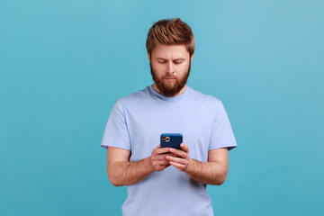 Wall Mural - portrait of serious concentrated bearded man texting message in social media on cell phone, using mo