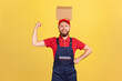 © khosrork - Portrait of strong courier man wearing blue uniform standing with cardboard box on his head, looking at camera, raised arm showing his power. Indoor studio shot isolated on yellow background.