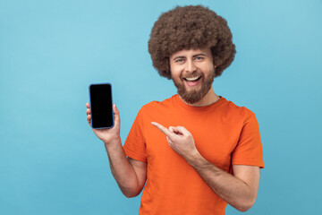 Wall Mural - portrait of smiling satisfied man with afro hairstyle wearing orange t-shirt pointing at mobile phon