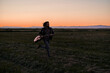 © FranciscoJavier - Caucasian young man with long hair in fur jacket running across the plain away from the mountains holding a guitar at sunset