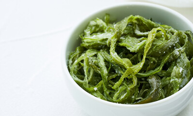 Wall Mural - heap of fresh Korean salted seaweed salad stem side dish or Miyeok Julgi Bokkeum in white bowl on white background. Laminaria or Kelp Seaweed stem                          