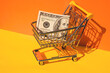 US dollar paper currency 100 banknote money Shopping trolley cart on colorful orange yellow background. Copy space for your text. Online shopping, buy mall market shop consumer concept. Small toy