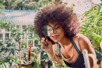 Woman, gardening and farmer with magnifying glass for carbon capture, plants or flower growth in outdoor garden. Black woman, nature and earth day or natural agriculture sustainability greenhouse