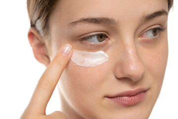 Wall Mural - Beauty young smiling woman applying cosmetic cream under her eye on a white background