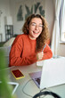 © insta_photos - Happy young woman student laughing using laptop sitting at desk studying online, looking at camera. Elearning concept. Virtual education classes, remote work and business webinars. Vertical portrait.