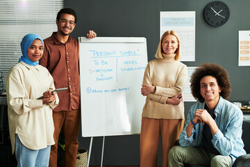 Poster - Several happy young intercultural students and mature blond teacher surrounding whiteboard with explanation of Present Simple tense