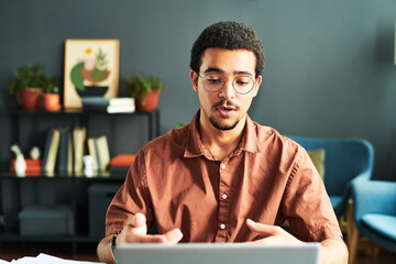Poster - Young businessman or online student or tutor communicating with online audience while sitting by workplace in front of laptop