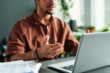 Poster - Focus on hand of young male tutor or student explaining something during online lesson while sitting by desk in front of laptop screen