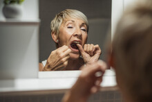 Mature Woman Is Using Dental Floss To Clean Her Teeth.