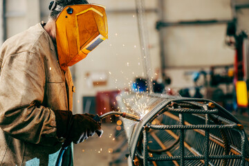 Wall Mural - Profile of a metallurgy worker welding metal framework while standing facility.