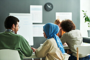 Poster - Back view of two young intercultural students discussing new subject in front of camera against other learner consulting with teacher