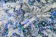 Snowy Christmas tree shiny blurry background with festive twinkling garlands lights. Garland lights between the snow-covered frosty white branches of the Christmas tree. White-blue frosty background.