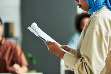 Poster - Close-up of young Muslim female speaker with document making report at conference or seminar while standing against audience