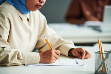 Poster - Hand of young Muslim female student with pencil over paper with grammar test ticking right answers during individual work