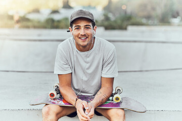 Young man, skateboard and skater with music at urban skate park, youth and recreation with earphones for audio streaming. Happy, portrait, and gen z outdoor with skating practice and fitness.