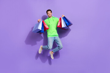 Poster - Full length photo of cute impressed guy dressed neon sweatshirt jumping high rising shoppers isolated violet color background