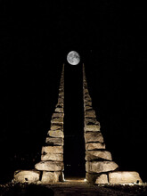 Artistic Photo Of Two Giant Cairns, Illuminated At Night By Spotlights, With A Pyramidal And Symmetrical Structure, Pointing Towards A Pretty View Of The Full Moon And A Starry Black Sky.