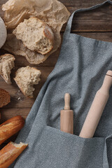 Poster - Clean kitchen apron with rolling pins and different types of bread on wooden table, flat lay