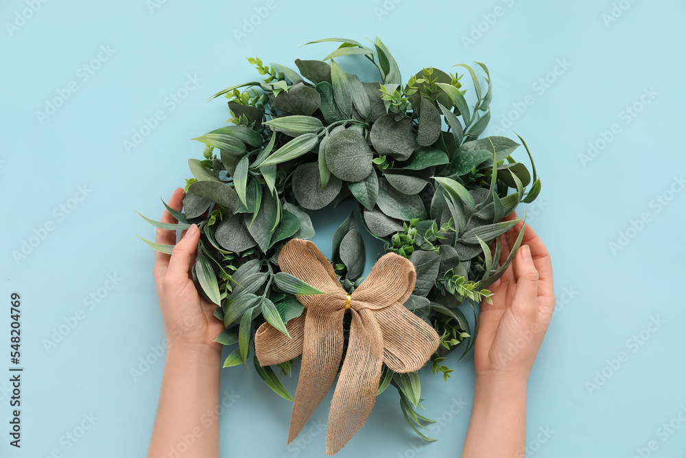 Female hands with stylish Christmas wreath on color background