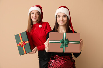 Sticker - Young women in Santa hats with Christmas gifts on beige background