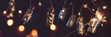 Christmas Garland With Golden Lights In Darkness. String Of Lights In Glass Cylinders With Sparkler And Bokeh. Abstract Christmas Background With Short Depth Of Field.