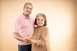 © GAJENDRRA BHATI  - Happy indian senior couple in love looking at each other hand while dancing together isolated over beige studio background, two pensioners husband wife enjoying life moments on retirement.