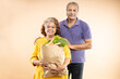 © GAJENDRRA BHATI  - Happy senior indian couple hold grocery paper bags with food isolated on beige background. studio shot. Retirement life.
