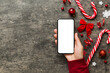 © sosiukin - christmas mockup with space for text. christmas advertising, app template. hand holding phone with empty screen on table background. Happy New Year and Xmas Flat lay