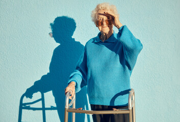 Portrait, shadow and disability with a senior woman on a blue wall background while holding a mobility walker outdoor. Health, handicap and fashion with a mature female standing outside alone