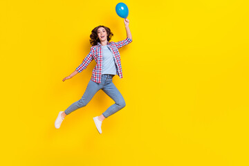 Sticker - Full size photo of satisfied good mood woman curly hair checkered shirt flying hold blue air bubble isolated on yellow color background