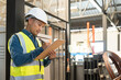 © Natee Meepian - Asian man wearing reflective jacket holding checklist paper standing in factory warehouse.