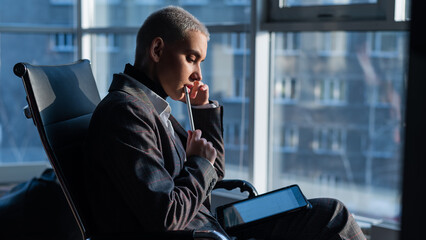 Business woman with short hair sits by the window and writes on a digital tablet with a stylus pen