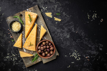 Wall Mural - Parmesan cheese on a wooden board, Hard cheese, olives, rosemary on a dark background. place for text, top view