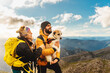 couple of hikers doing a mountain route with their dog. Mountaineer holding his dog in his arms with a mountain range landscape in the background.