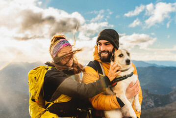 couple of hikers in the rain making a mountain route with their dog. Mountaineer holding his dog in his arms with a mountain range landscape in the background. woman petting dog