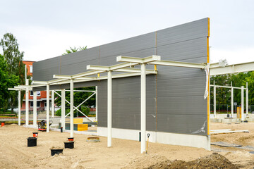 Canvas Print - Unfinished steel construction frame of a new modern warehouse with gray sandwich panel wall