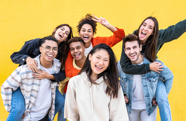 Diverse community of young people smiling together on a yellow wall background - Multiracial college students having fun laughing outside - Youth culture concept