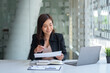 © amnaj - Asian businesswoman sitting happily with her laptop and takes notes intensely and smiles happily at her assignment.