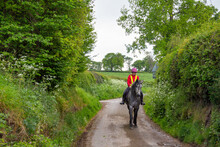 Young Woman And Her Horse Hacking In The English Countryside, Wearing Brightly Coloured Safety Gear To Ensure They Are Seen By Other Road Users , Keeping Everyone Safe On The Roads.
