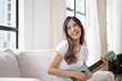 Happy asian women enjoy singing by playing guitar, ukulele while sitting on sofa at home.