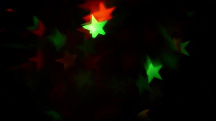 Wall Mural - Abstract background of Christmas bokeh stars. Red and green stars flicker and fading on a black background. Festive mood background can be used as a transition or overlay.