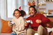 © JenkoAtaman - African american family father and daughter laugh and play video games together using a video game console on christmas holiday