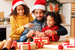 © JenkoAtaman - Happy ethnic family father and children pack Christmas gifts