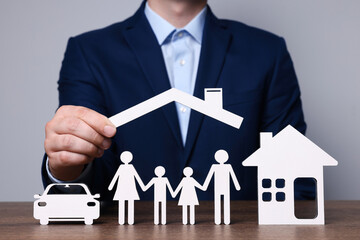 Man holding figure of roof above family at wooden table. closeup. Insurance concept