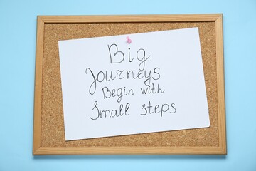 Wall Mural - Corkboard with pinned message Big Journeys Begin With Small Steps on light blue background, top view. Motivational quote